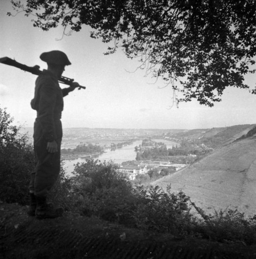 A photo by CFPU photographer Lt. Ken Bell, who has posed Sergeant B. Shaw of Québec City holding a Bren gun overlooking ROUEN, France, and the River Seine on 31 August 1944.